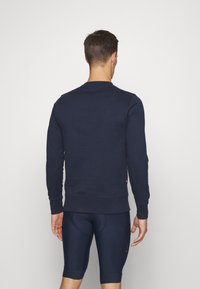 Felpa in cotone blu navy con colletto a giro e polsini a costine, indossata da un modello, che mostra un design semplice e aderente.
