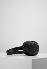 Bolso de cinturón negro de piel acolchada con forma redonda, cierre de cremallera y correa ajustable. Textura suave con acentos sutiles para mayor durabilidad.