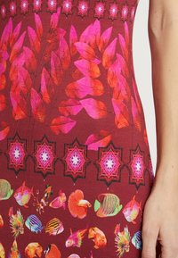 Multicolored dress featuring a floral and fish pattern, with red, pink, and black hues, and textured detailing.