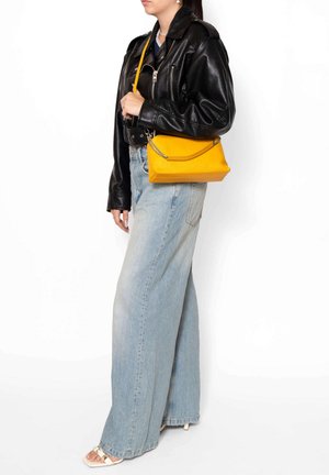 Sac à main en cuir jaune avec une finition texturée, fermeture éclair et accent chaîne en argent. Porté avec une veste en cuir noire et un jean à jambes larges.