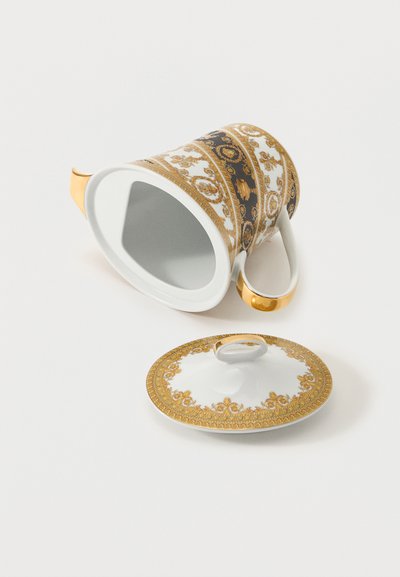 Λευκό τσαγιερό από πορσελάνη με περίτεχνα χρυσά σχέδια και μαύρες ζώνες, που βρίσκεται σε πλάγια θέση δίπλα στο αντίστοιχο καπάκι του με χρυσή διακόσμηση, πάνω σε λευκή επιφάνεια.