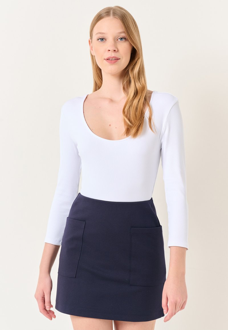 Biały prążkowany body z długim rękawem w zestawie z granatową mini spódnicą z dwoma przednimi kieszeniami i prostym wykończeniem.