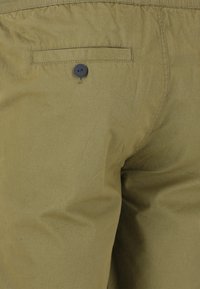 Olijfgroene katoenen broek met een gladde textuur, voorzien van een achterzak en een zwarte knoopsluiting voor een veilige sluiting.