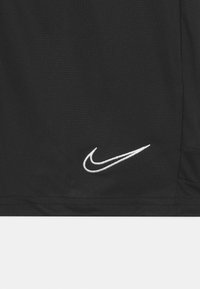 Svart tygtröja med korta ärmar, standardpassform, och strukturerat material. Fäster en vit broderad Nike-swoosh-logotyp längst ner till vänster.