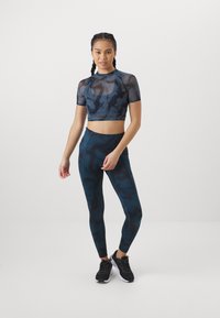 Haut de sport ajusté et coupé avec des manches courtes en matériau transparent bleu foncé, associé à un legging taille haute avec un motif abstrait bleu foncé.
