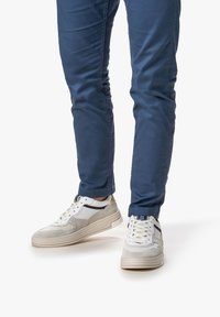 Sneaker bianche e beige con accenti in suede grigio, caratterizzate da un design elegante e materiali testurizzati, indossate con pantaloni blu navy.