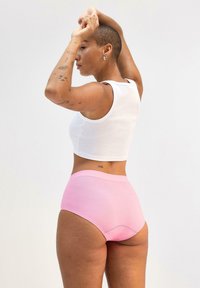 Höga underkläder i rosa bomull, kombinerade med en vit ribbad linne. Modellens tatuerade hud är synlig och framhäver detalj på armen.