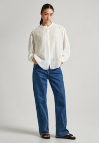 Camicetta bianca con maniche lunghe, abbinata a jeans in denim blu a vita alta. Adatta per un look casual con una silhouette rilassata. Sandali neri.