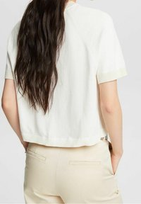 Biała bluzka z krótkim rękawem, z prążkowanym wykończeniem u dołu i na mankietach, w luźnym kroju i miękkiej teksturze, połączona z jasnobeżowymi spodniami.