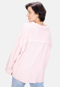 Light pink long-sleeve shirt made of textured fabric, featuring a loose fit, back yoke detail, and cuffs with buttons.