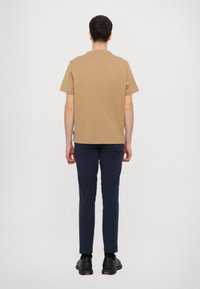 Brown short-sleeve T-shirt with a straight cut, paired with navy slim-fit trousers, and black sneakers with textured sole detail.