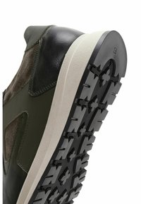 Zapatillas verdes y negras que combinan materiales de cuero y ante, con una suela de goma de alto contraste y un patrón de textura en la suela para mayor agarre.