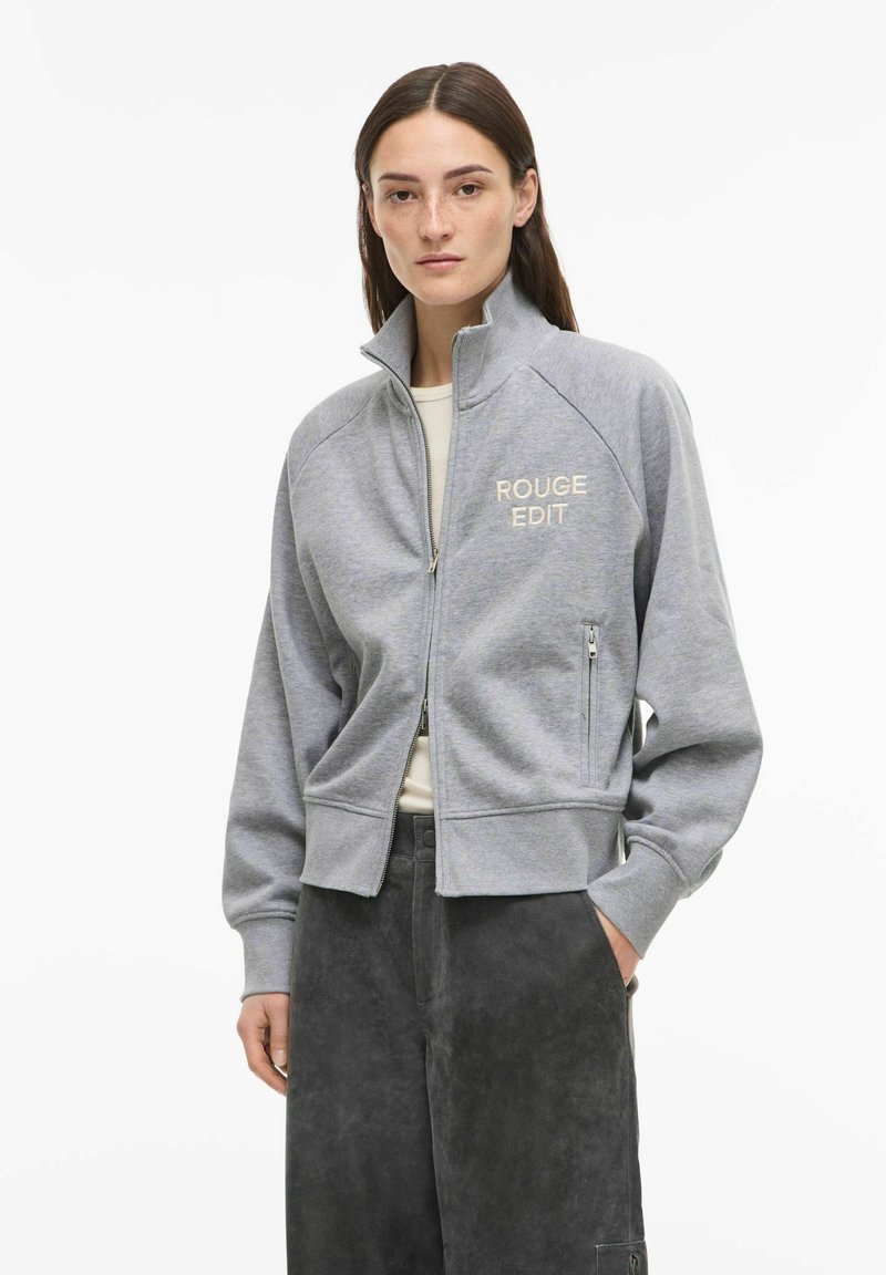 Grau melierter Sweatshirt mit Reißverschluss und hohem Kragen, mit der Aufschrift "ROUGE EDIT" in hellbeige, aus weichem Stoff mit gerippten Bündchen und Saum.