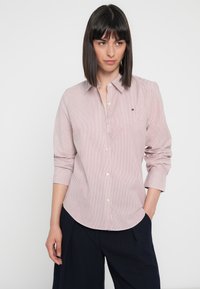 Chemise rayée à boutons rouge et blanc, avec des manches longues, un col classique et un petit logo brodé sur la poitrine.