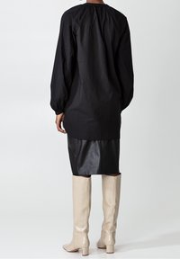 Svart oversized skjorta med långa puffärmar, samlad halsringning, i kombination med en figurnära svart läderkjol och knähöga beige stövlar.