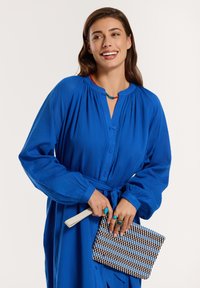 Világoskék gombos ruha, gyűrt dekoltázzsal és hosszú ujjakkal, deréknál behúzva. Kockás mintájú clutch táska és kiegészítők, köztük gyűrűk.
