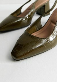 Tacchi slingback in vernice verde oliva con punta affusolata e motivo a coccodrillo testurizzato. Il tacco a blocco offre stabilità e supporto.