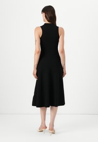 Svart ermeløs kjole med tettsittende bodice, utsvingt skjørt og glatt tekstur. Har rund halslinning og faller under kneet.