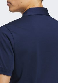 Mørk blå polo skjorte med klassisk krage og korte ermer. Glatt tekstur med en tettsittende design, vist fra baksiden.