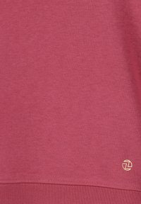 Rode sweater van zacht, textuurstof. Voorzien van ribgebreide manchetten en onderrand, met een klein gouden logo in de linkerbenedenhoek.