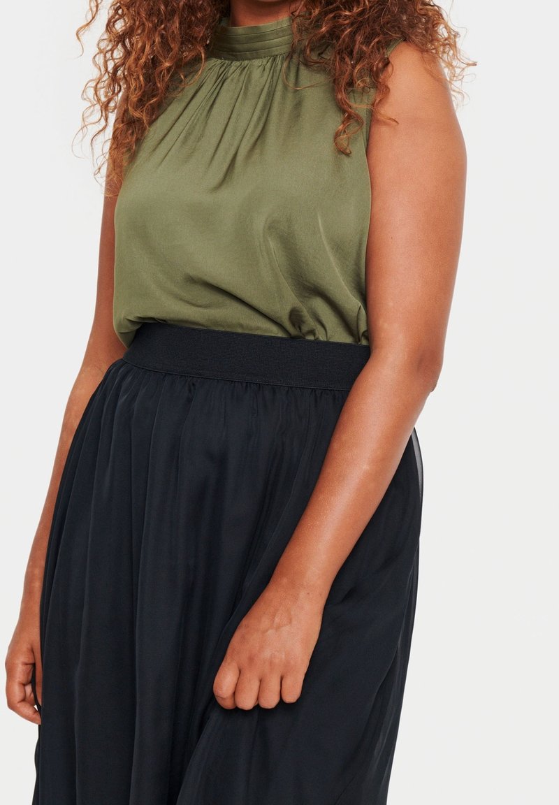 Olive green sleeveless top with gathered neckline paired with a black, flowy, pleated skirt featuring an elastic waistband.