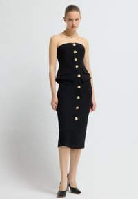 Černé šaty bez ramínek s přiléhavým korzetem, zlatými květinovými knoflíky a dvěma předními kapsami. Design zahrnuje peplum pas a siluetu tužkové sukně.