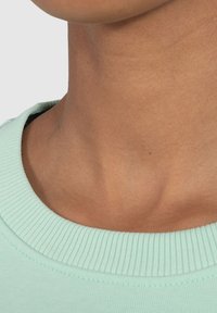 Collo verde menta con un bordo rigato, con una carnagione leggermente abbronzata sotto. Texture morbida visibile nella stoffa e nei contorni della pelle.