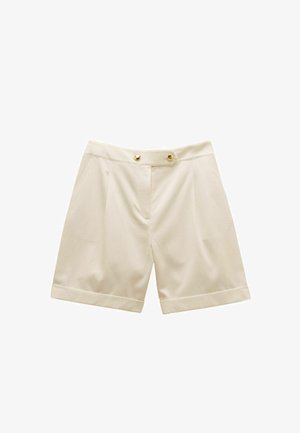 Augsti pieguļošas bēša krāsas šortus ar uzlocītām malām, priekšējām krokām, sānu kabatām un divām zelta pogām uz jostasvietas.