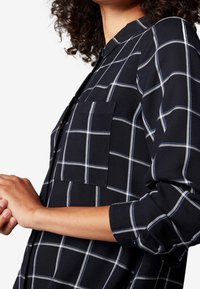 Marinblå rutig skjorta i mjukt material, med knappskyddad krage, långa ärmar och en enda bröstficka med vita rutmönster.