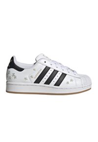 Valkoinen Adidas Superstar -tennarit mustilla raidoilla, pienillä kirjotuilla keltaisilla ja valkoisilla kukilla, kuorikärkisillä ja kumipohjaisilla kengillä.