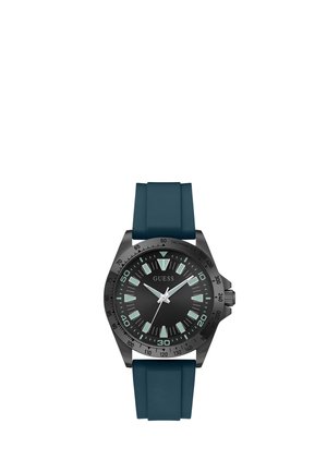 Montre Guess gris foncé avec cadran noir, index lumineux, lunette tachymétrique et bracelet en silicone bleu foncé.