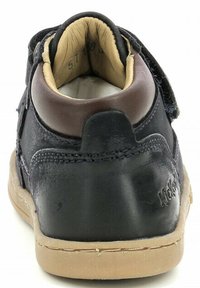 Zapato de cuero azul marino con un cuello acolchado marrón, cierre de velcro, suela de goma beige y detalles de costura visibles. El interior muestra un forro suave.