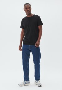 Sort bomulds T-shirt med rund halsudskæring, parret med blå denim jeans og sølvfarvede træningssko med hvide og sorte accenter.