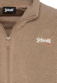 Giacca in pile beige con zip frontale, collo alto e logo ricamato bianco sul lato sinistro del petto. Materiale morbido e dalla texture piacevole.