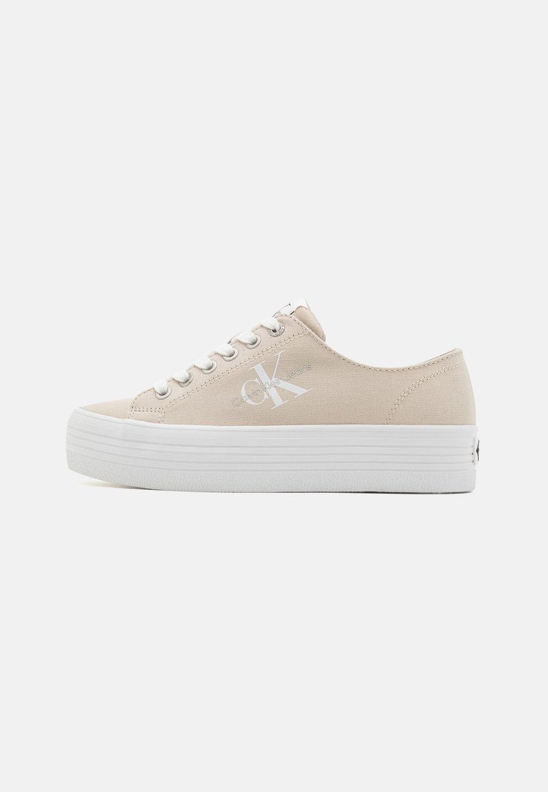 Beige Leinensneaker mit weißen Gummi-sohlen, ausgestattet mit einer erhöhten Plattform, runder Zehenpartie und einem seitlichen Logo-Druck. Metallische Ösen mit Schnürsenkeln.