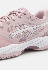 Sapatilha atlética rosa claro com um cabedal sintético texturizado, painéis em malha, detalhes brancos e uma sola branca curva. Cadarços e logotipo visíveis.