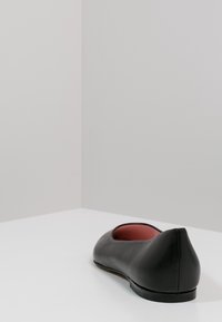 Bailarina de cuero negra con punta redondeada, interior rojo y acabado mate. La suela es plana y ligeramente elevada en la parte trasera.