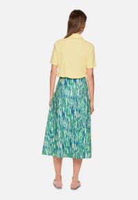 Gelbes Poloshirt mit kurzen Ärmeln, kombiniert mit einem grünen Rock mit blau-weißem abstraktem Muster, knielang.