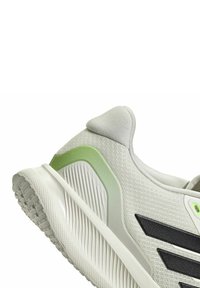 Zapatilla deportiva gris claro con rayas negras y detalles verdes. Presenta una parte superior texturizada y una suela contorneada para estabilidad.