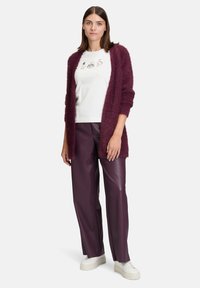 Burgundowa, futrzasta kardigan na białym t-shircie z graficznymi nadrukami, w zestawie z cygaretkami z sztucznej skóry w kolorze śliwkowym o wysokim stanie i białymi trampkami.