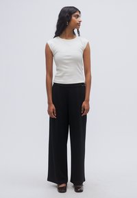 Φόρεμα κοντομάνικο σε ανοιχτό γκρι χρώμα, συνδυασμένο με μαύρο παντελόνι φαρδύ με ψηλή μέση και καφέ επίπεδα παπούτσια. Απλές, καθαρές γραμμές.