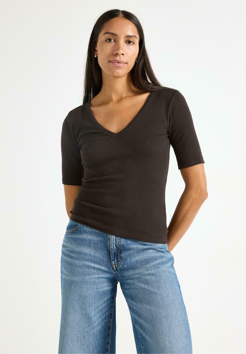 Top a maniche corte a V in cotone marrone a coste abbinato a jeans a gamba larga blu chiaro, che mette in evidenza una silhouette aderente e una texture morbida.