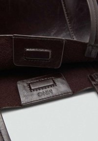 Cuoio marrone scuro con una finitura testurizzata e cuciture visibili; include un'etichetta impresso con "MNG" su una patch rettangolare liscia.