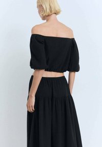 Schwarzes Off-Shoulder-Top mit puffärmel und taillierter Passform, aus strukturiertem Stoff hergestellt. Kombiniert mit einem passenden, gestuften Rock.