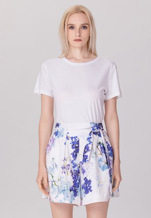 T-shirt blanc à manches courtes associé à une jupe florale taille haute avec des motifs bleus et violets, dotée d'un détail de ceinture nouée à la taille.
