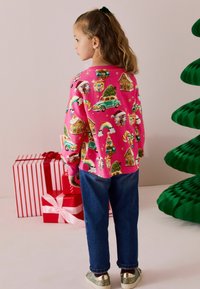 Camicia a maniche lunghe rosa con motivi colorati a tema festivo. Abbinata a jeans blu e sneakers lucidi e glitterati. Vista posteriore di un bambino.