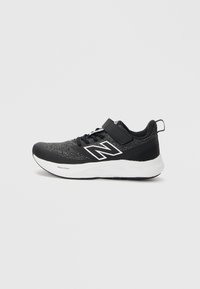 Chaussure de sport noire avec une tige texturée, accents blancs et une sangle sur les lacets. Elle présente une semelle rembourrée pour plus de confort.