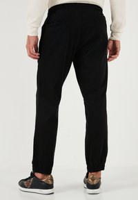 Schwarze, elastische Jogginghosen in slim fit, ausgestattet mit Seitentaschen und verstellbaren Bündchen, kombiniert mit schwarzen Sneakers mit goldenen Akzenten.