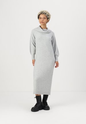 Robe en tricot grise avec un col cheminée, de longues manches bouffantes et des poignets côtelés, associée à des bottes de combat noires à lacets.