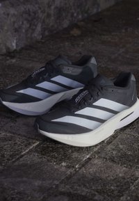 Par sorte og hvide Adidas Adizero løbesko placeret på en struktureret stensål.